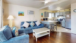 A living room with a sofa, a coffee table, and a kitchen area with cabinets and appliances. - Condo Less than Two Miles to the Ocean with Pool, Fast WiFi, and Private W/D (Ocean City)