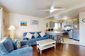 A living room with a sofa, a coffee table, and a kitchen area with cabinets and appliances. - Condo Less than Two Miles to the Ocean with Pool, Fast WiFi, and Private W/D (Ocean City)