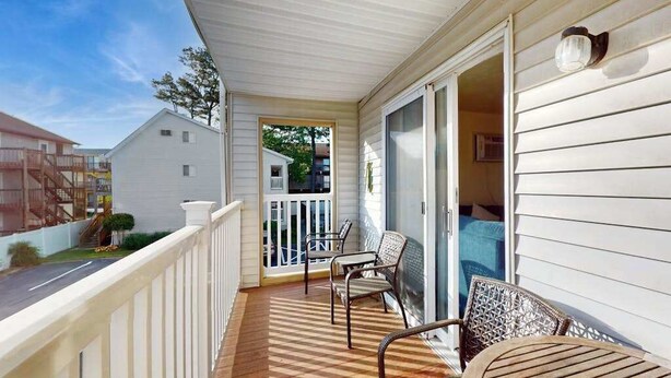 A covered porch with a railing, two chairs, and a table. - Condo Less than Two Miles to the Ocean with Pool, Fast WiFi, and Private W/D (Ocean City)