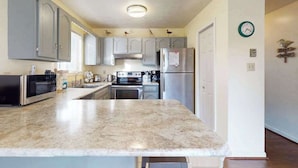 A kitchen with grey cabinets, a stainless steel refrigerator, a microwave, and a coffee maker. - Condo Less than Two Miles to the Ocean with Pool, Fast WiFi, and Private W/D (Ocean City)