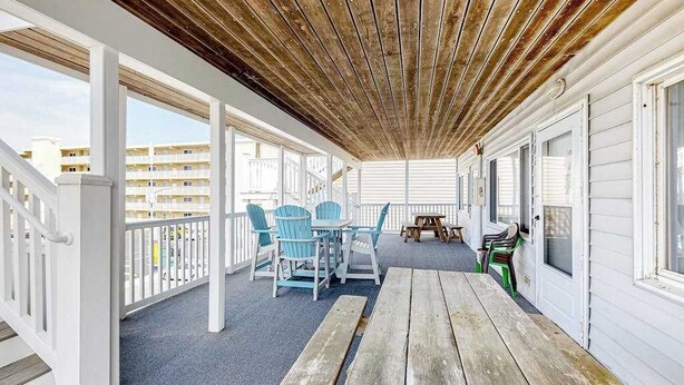 Un espace extérieur abrité, doté d’un plafond en bois, de rampes blanches et d’une table avec des chaises.