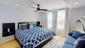 Une chambre à coucher comprenant un lit, un ventilateur de plafond, une table de chevet, une commode, un canapé et une fenêtre avec des rideaux.