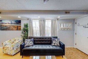 A living room with a black sofa, a patterned bean bag, a large painting, and a wall with a decorative sign. - The Quarterdeck Ocean Block (Ocean City)