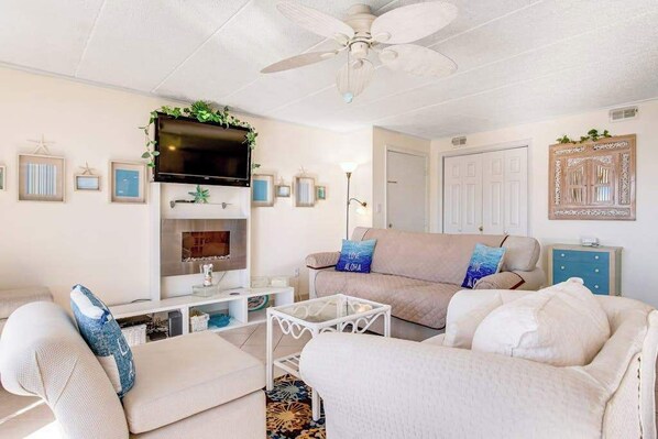A living room with a ceiling fan, a flat-screen TV, a beige sofa, a white armchair, and a coffee table. - Thunder Island 83B (Ocean City)