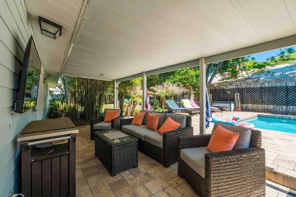 A covered patio area with wicker furniture, a pool, and a view of the backyard.