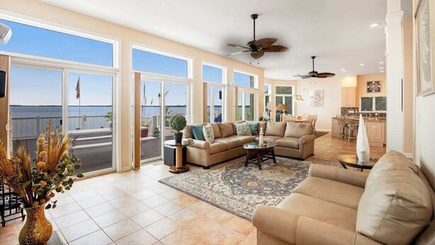 A spacious living area with a large window, a ceiling fan, and a view of the ocean. - A Bayfront Row Seat (Ocean City)