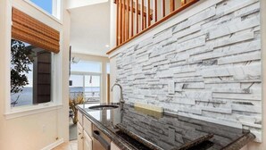 A kitchen with a stone backsplash, a window with a view, and a wooden staircase. - A Bayfront Row Seat (Ocean City)