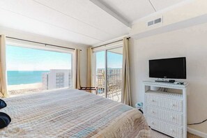 A bedroom with a bed, a TV on a white dresser, and a balcony with a view of the sea. - Excalibur 905 (Ocean City)