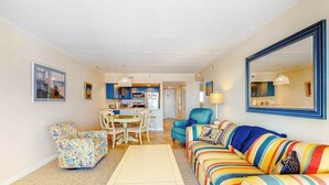 A living room with a sofa, armchair, coffee table, and a dining area with chairs and a table. - Excalibur 905 (Ocean City)