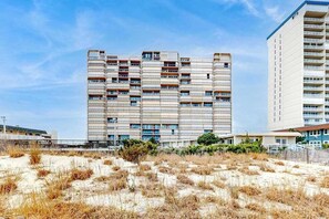 A multi-story building with a flat facade, balconies, and a sandy foreground. - Fountainhead Towers 506 (Ocean City)