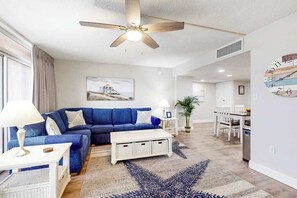 A modern living room with a blue sofa, white coffee table, and a ceiling fan. - Fountainhead Towers 506 (Ocean City)