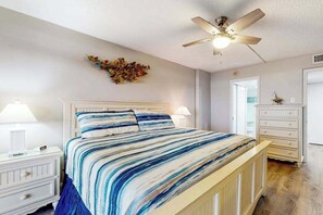 A bedroom with a bed, nightstands, a dresser, a ceiling fan, and a wall decoration. - Fountainhead Towers 506 (Ocean City)