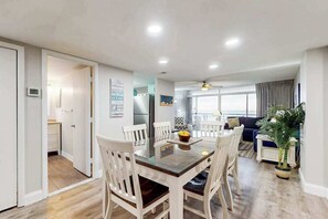 A modern living room with a dining area, a ceiling fan, and a large window. - Fountainhead Towers 506 (Ocean City)