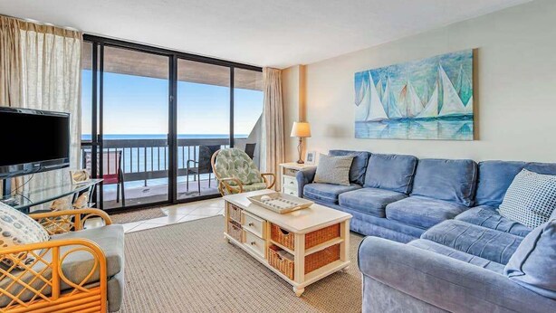 A living room with a sofa, a television, a coffee table, and a painting. - 22nd-Floor Oceanfront Gem with Three Balconies, W/D, AC, and Shared Heated Pool (Ocean City)