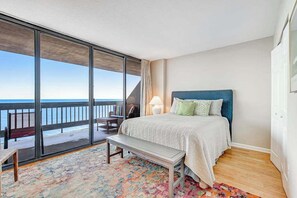 A bedroom with a large window, a bed, a bench, and a view of the ocean. - 22nd-Floor Oceanfront Gem with Three Balconies, W/D, AC, and Shared Heated Pool (Ocean City)