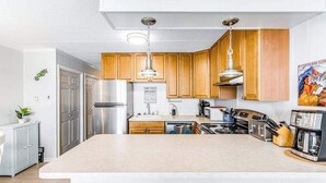 A modern kitchen with wooden cabinets, stainless steel appliances, and a central island with seating. - Condesa 201 (Ocean City)