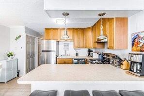 A modern kitchen with wooden cabinets, stainless steel appliances, and a central island with seating. - Bright, sunny condo with ocean and bay views in walkable Midtown location (Ocean City)