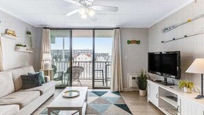 A modern living room with a sofa, coffee table, TV, and balcony with a city view. - Condesa 201 (Ocean City)