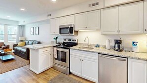 A modern kitchen with white cabinets, stainless steel appliances, and a granite countertop. - Bay Island 4 (Ocean City)