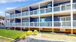 A multi-story building with balconies, a paved driveway, and a grassy area with small bushes. - Bay Island 4 (Ocean City)