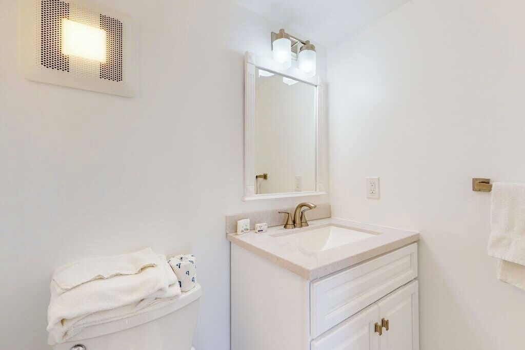 Une salle de bain équipée d’un lavabo, d’un miroir, d’un porte-serviettes et d’un luminaire fixé au mur.