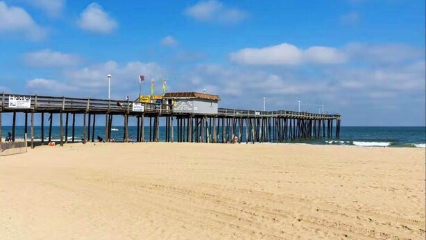 A beach with a wooden pier extending into the ocean, a building on the pier, and a clear sky. - Bay Island 4 (Ocean City)