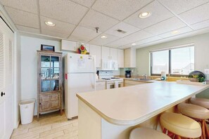 A kitchen with a central island, white cabinets, a refrigerator, and a window providing natural light. - Waikiki 406 (Ocean City)