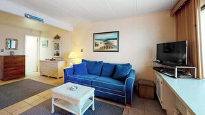 En stue med en blå sofa, et lille hvidt bord, et fjernsyn og et skab.