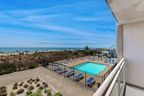 A pool area with sun loungers, a clear view of the beach, and a fenced pool. - Oceanfront Condo with Balcony, WiFi, W/D & Shared Pool - Close to Boardwalk (Ocean City)