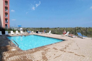 A swimming pool with lounge chairs and a fence, a building with balconies, and a clear sky. - Oceanfront Condo with Balcony, WiFi, W/D & Shared Pool - Close to Boardwalk (Ocean City)