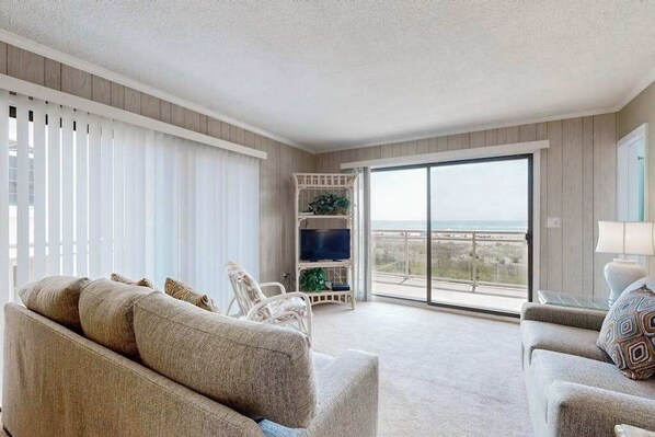 A spacious living room with a sofa, armchairs, a TV, and a balcony with a view. - Oceanfront Condo with Balcony, WiFi, W/D & Shared Pool - Close to Boardwalk (Ocean City)