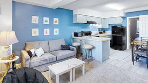 Ein gemütlicher Wohnbereich mit Küchenzeile, einer Couch, einem Couchtisch und Bildern an der Wand.
