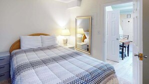 Ein Schlafzimmer mit einem Bett, Nachttischlampen, einem Spiegel und einer Tür zu einem Essbereich.