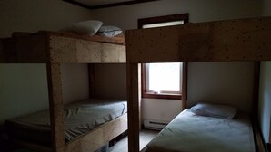 Habitación con literas, ventana, radiador y un cubo de basura verde.