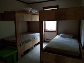 A bunk bed room with a window, a radiator, and a green trash bin.