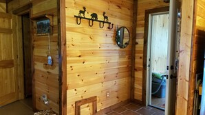 Interior de madera con un banco, una mesita, un espejo colgado en la pared y una puerta que da a otra habitación.
