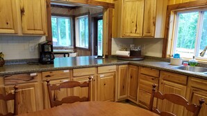 Una cocina con armarios de madera, encimera de granito, una mesa de comedor con sillas y una ventana con vista a árboles.