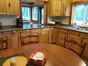 A kitchen with wooden cabinets, a granite countertop, a dining table with chairs, and a window with a view of trees.