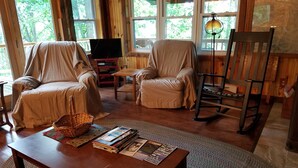 Una sala de estar acogedora con dos sillones, una mesa de centro de madera, un televisor y un sillón mecedor.