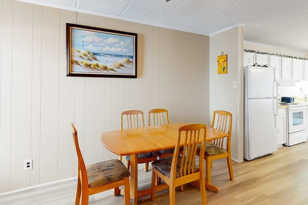 Un coin repas avec une table et des chaises en bois, un réfrigérateur blanc et un tableau accroché au mur.