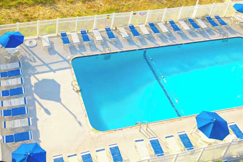 A rectangular pool with blue water, surrounded by white railings and blue lounge chairs.