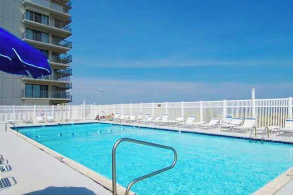 A swimming pool with lounge chairs and a white fence.