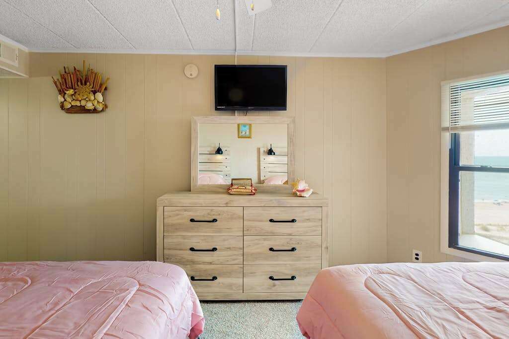 A bedroom with two beds, a dresser, a TV, and a window with a view.