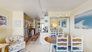 Ein Wohnzimmer mit Sofa, Esstisch und Stühlen, eine Küche mit Geräten sowie ein Flur, der zu einem weiteren Raum führt.