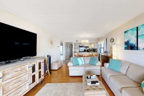 A living room with a large flat-screen TV, a sofa, a coffee table, and a dining area in the background. - Waterfront condo with effortless beach access, private balcony, games, W/D, & AC (Ocean City)