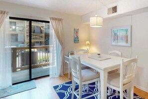 A dining area with a white table and chairs, a blue patterned rug, a hanging light fixture, and a view through a glass door. - Serene condo with central AC, deck & washer/dryer - near golf (Ocean City)