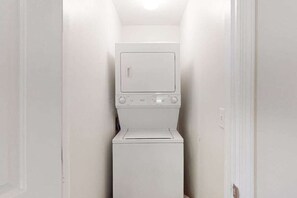 Une petite buanderie équipée d’un lave-linge et d’un sèche-linge à chargement frontal, avec une porte sur le côté droit et un luminaire au plafond.