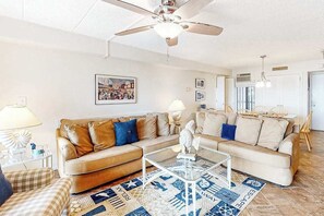 A living room with a beige sofa, a glass coffee table, a patterned rug, and a ceiling fan. - High Point South 4F (Ocean City)