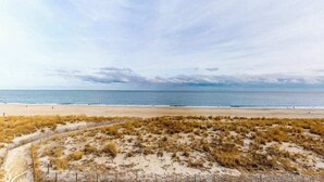Una playa con un sendero de arena y dunas cubiertas de hierba, que conducen al océano.