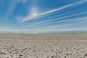 A wide sandy beach with footprints, a clear sky, and distant ocean waves. - Fantastic condo situated in beachfront condo with free WiFi & shared pool (Ocean City)